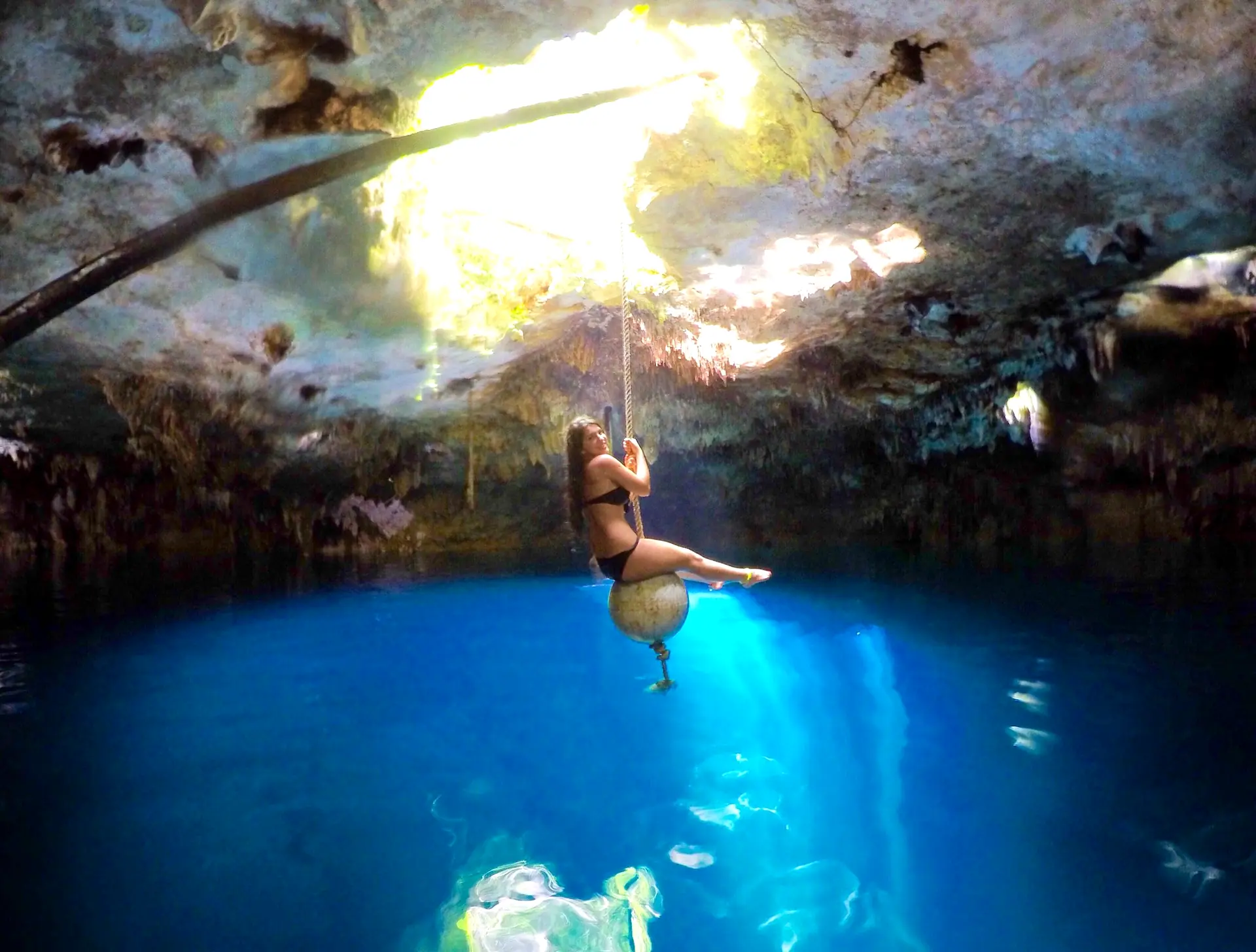 Visitante en el columpio sobre el agua azul de la cueva del cenote Kin-Ha